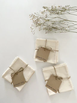 A stack of rustic linen napkins with simple, earthy-toned monograms, styled on a wooden farmhouse table.