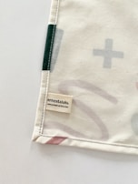 A corner of a fabric piece with an attached label displaying the text 'ernest & lulu' and a website URL. The fabric features printed abstract shapes in soft colors, bordered by stitching.