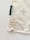 A corner of a fabric piece with an attached label displaying the text 'ernest & lulu' and a website URL. The fabric features printed abstract shapes in soft colors, bordered by stitching.