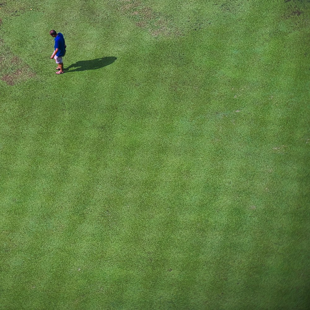 person in blue shirt and blue pants walking on green grass field during daytime