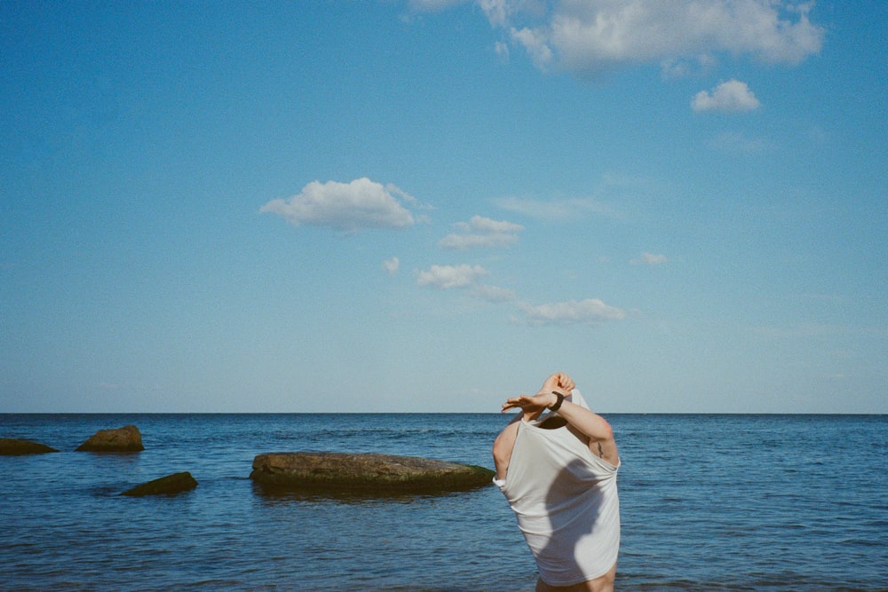 Frau in weißem Kleid, die tagsüber auf einem braunen Felsen in der Nähe eines Gewässers steht