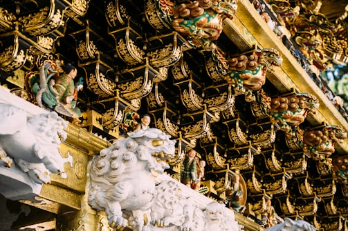 Intricately carved figures and ornate decorations adorn the roof of a traditional structure. The detailed craftsmanship features mythological creatures and small human figurines amidst elaborate golden patterns.