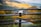 A drone is hovering outdoors against a scenic backdrop of hills and a blurred background. The focus is on the drone, with its rotors spinning and a metallic finish.