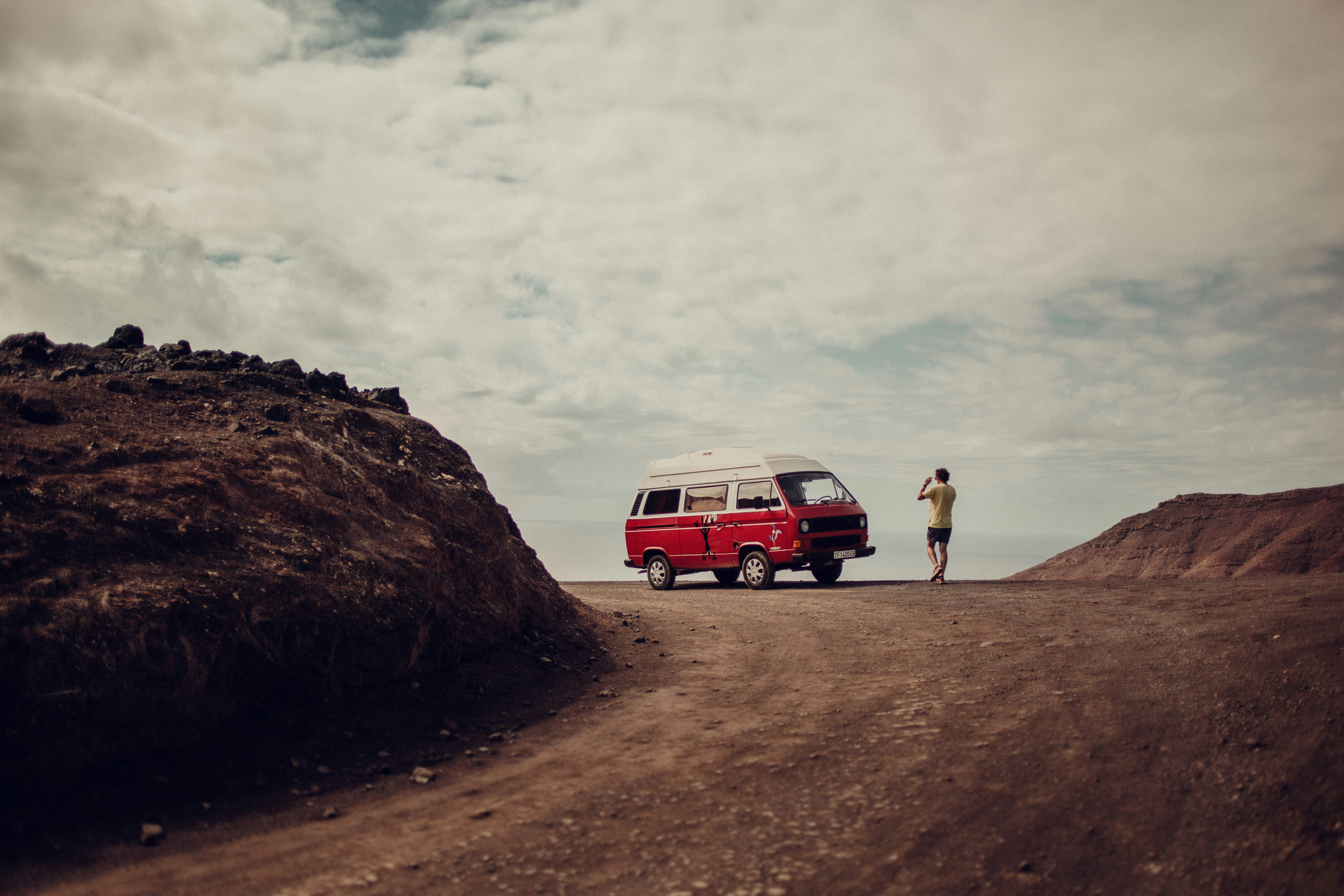 man in black jacket standing beside red and white suv during daytime, 
