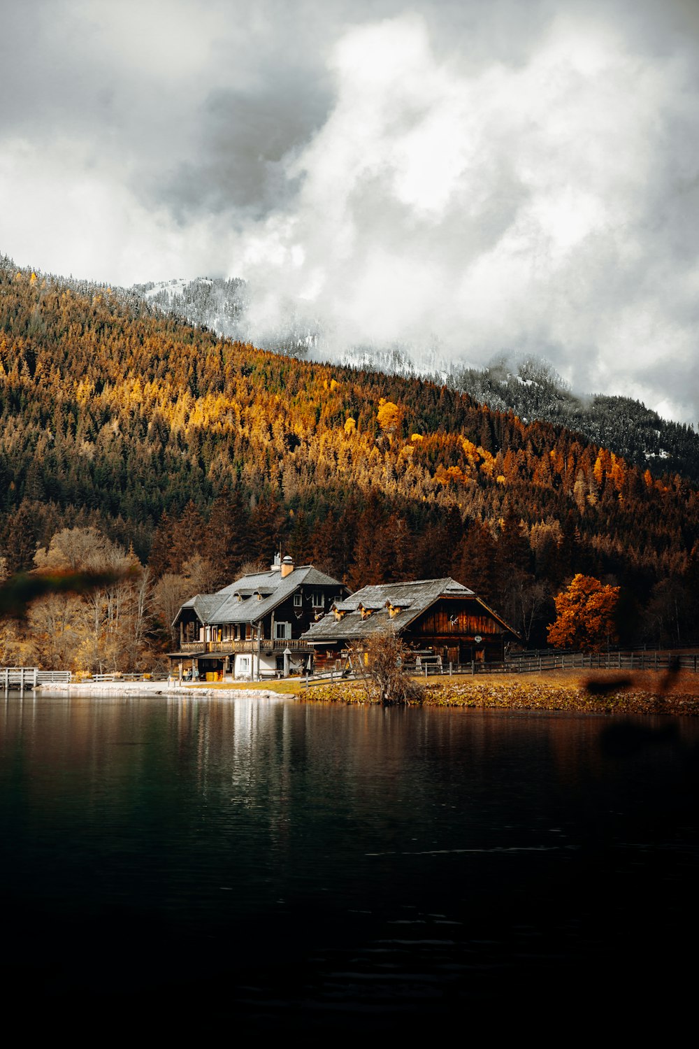 white and brown house near lake and green trees under white clouds and blue sky during