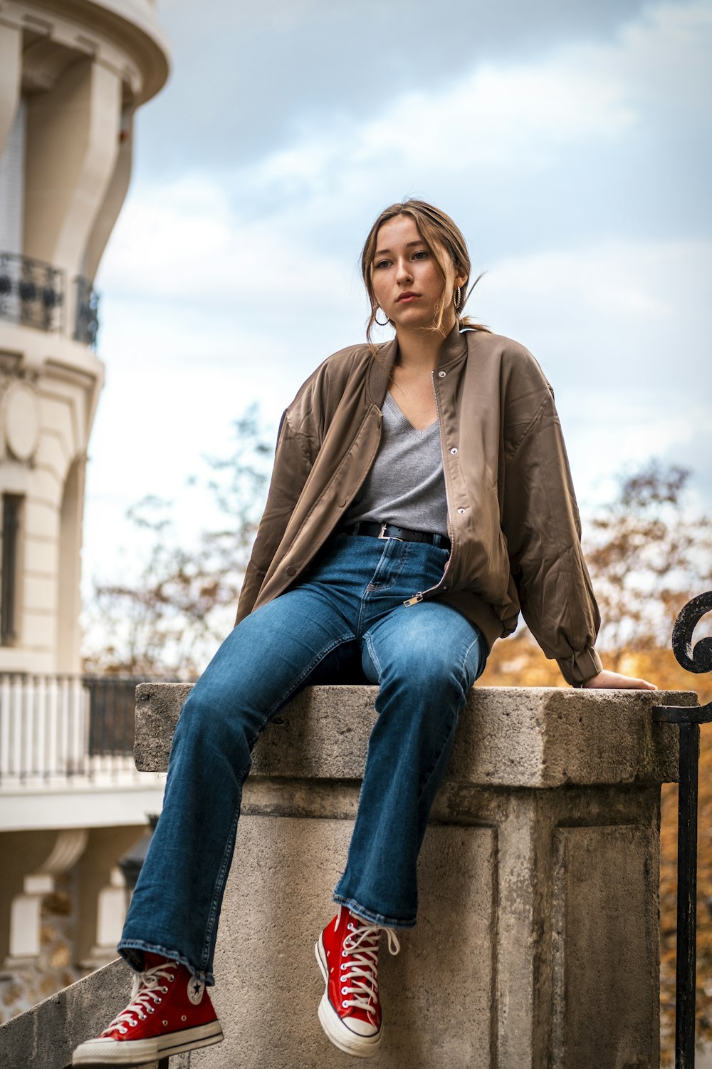 woman in brown jacket and blue denim jeans sitting on brown concrete bench during daytime