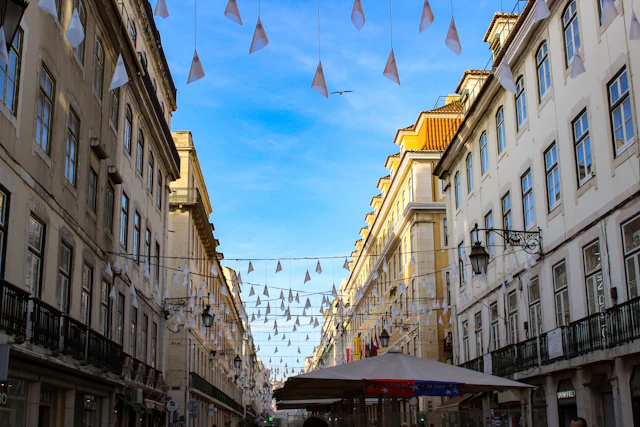 A pedestrian street in Baixa strung with decorative hanging lights between pastel-colored facades