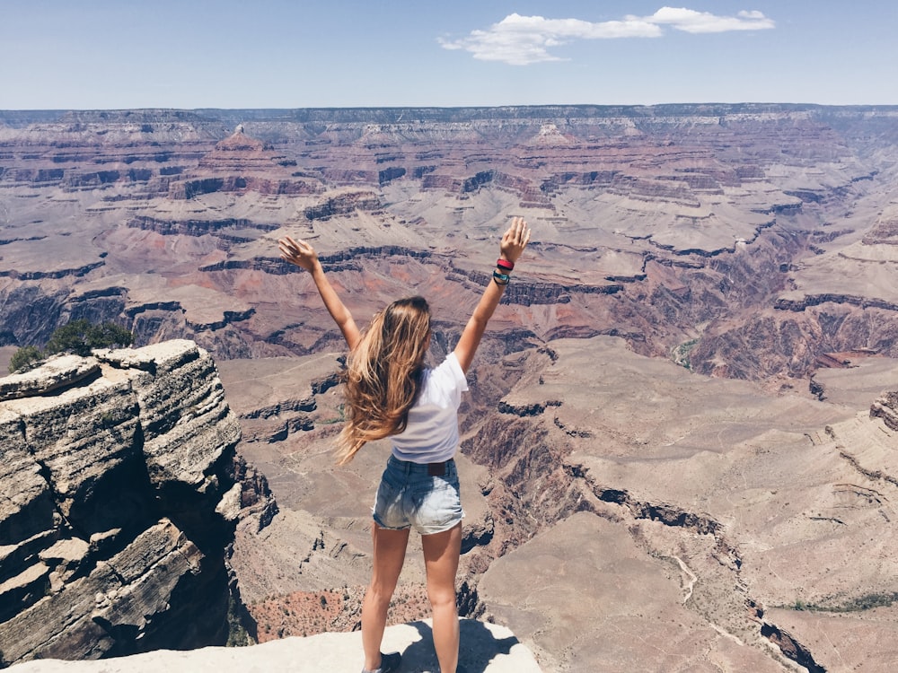 woman in white t-shirt and blue denim shorts standing on rocky hill during daytime