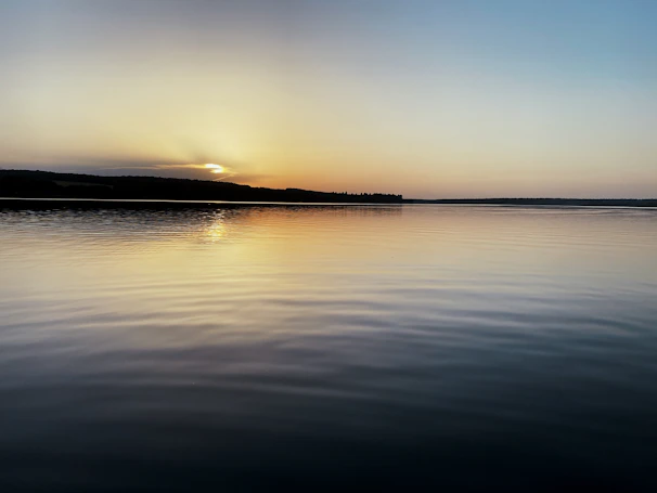 A peaceful sunset casting deep indigo hues over a calm lake horizon.