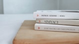 Three books are stacked on a wooden surface, with their spines partially visible. The names on the spines suggest they are foreign language books. Light colors dominate the scene, giving it a clean and minimalistic look.
