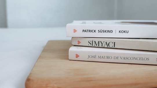 Three books are stacked on a wooden surface, with their spines partially visible. The names on the spines suggest they are foreign language books. Light colors dominate the scene, giving it a clean and minimalistic look.