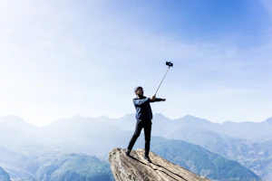 A vibrant selfie stick extended on a mountain trail with a sunset backdrop