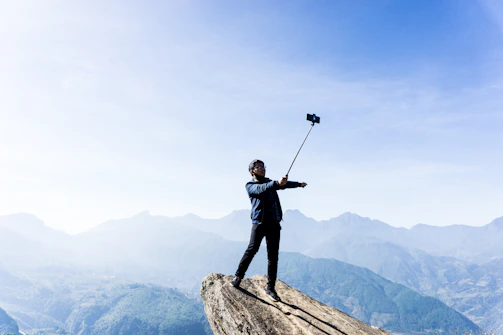 A vibrant selfie stick extended on a mountain trail with a sunset backdrop