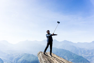 A selfie stick extended on a mountain trail with a hiker capturing the view.