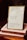 A framed quote board is resting on two stacked books with handwritten notes. The frame contains three quotes: one referencing Buethech, another citing Proverbs 31:25 about strength and dignity, and the third quoting John 16:33 about peace. The books are labeled 'MONTH 3: TRUE IDENTITY' and 'MONTH 3: IDENTITY.'