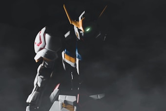 A large robot with angular and armored features is positioned in a dark and misty environment. It has prominent horns on its head and a glowing green eye, with its body showing white, blue, and red accents.