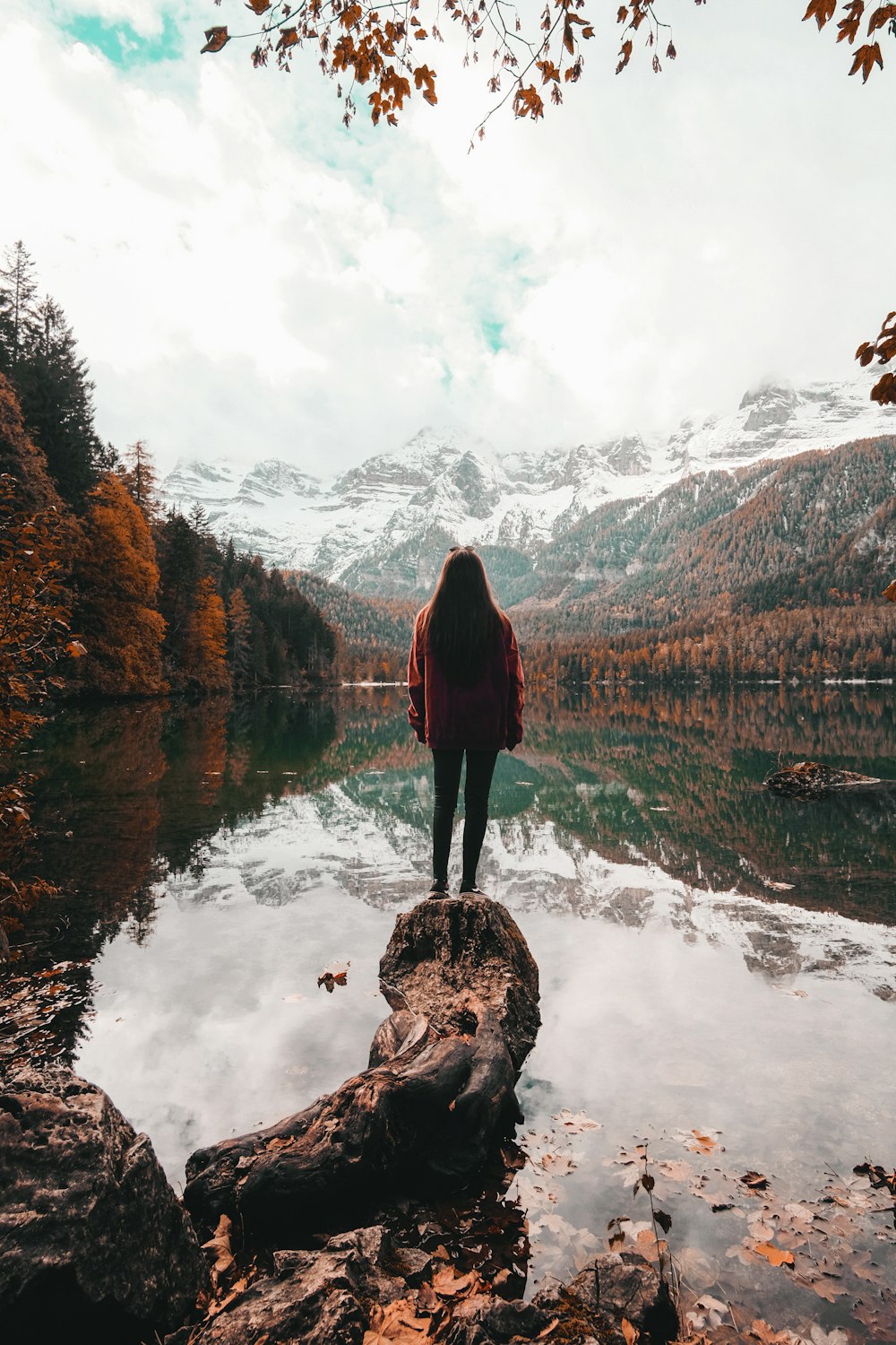 woman in black jacket standing on rock near lake during daytime