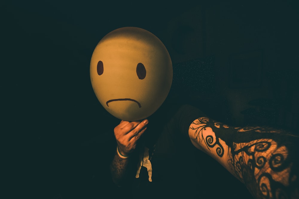 person holding yellow and black smiley balloon