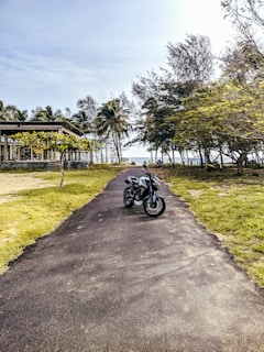 Close-up of a motorbike parked on a sandy path, framed by tropical foliage and a glimpse of the ocean beyond.