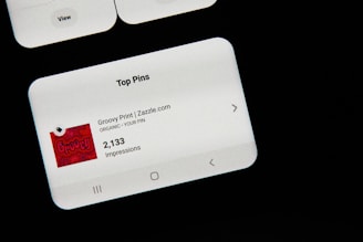 A smartphone screen displaying the 'Top Pins' section on a social media app. The focus is on a pin titled 'Groovy Print | Zazzle.com', which has 2,133 impressions. The background is mostly dark, highlighting the white interface elements on the screen.