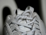 Close-up view of a white sneaker's laces, showing intricate details of the woven texture and stitching on the leather material.