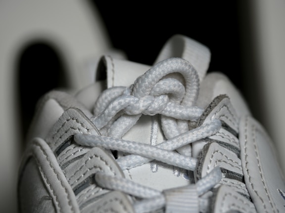 Close-up view of a white sneaker's laces, showing intricate details of the woven texture and stitching on the leather material.