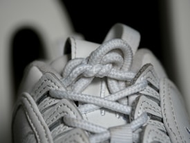 Close-up view of a white sneaker's laces, showing intricate details of the woven texture and stitching on the leather material.