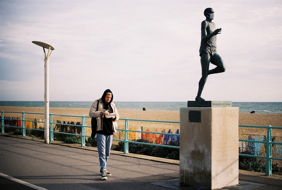 man in black jacket and blue denim jeans standing beside statue during daytime