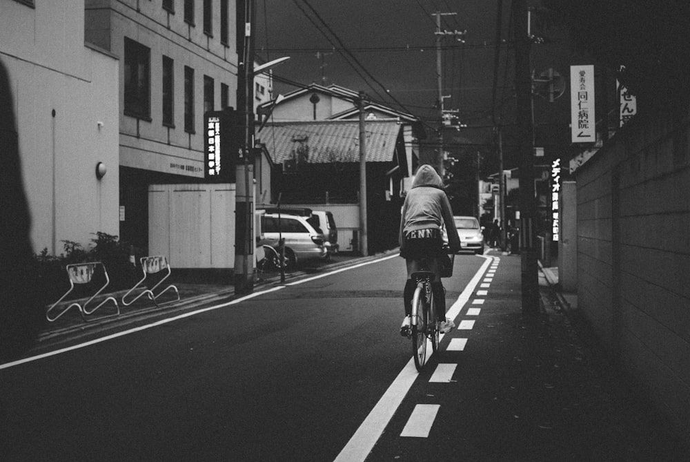 grayscale photo of man riding bicycle on road