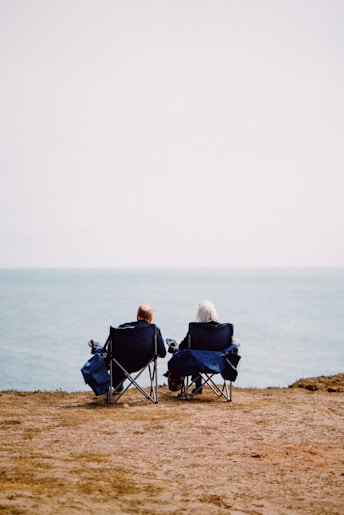 2 person sitting on blue camping chairs on brown field during daytime