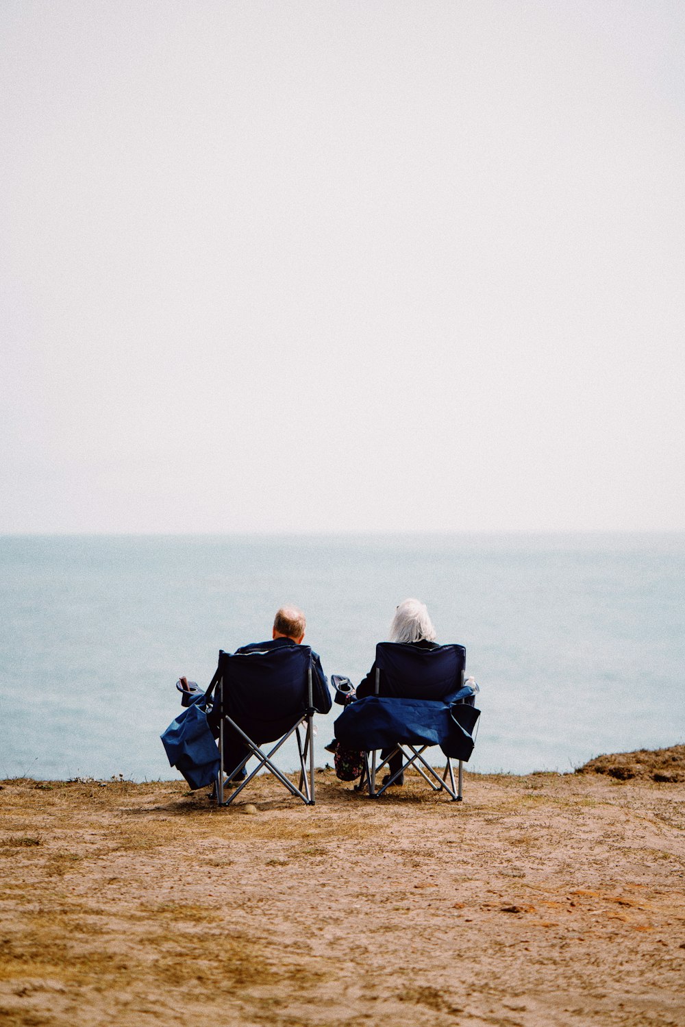 2 person sitting on blue camping chairs on brown field during daytime