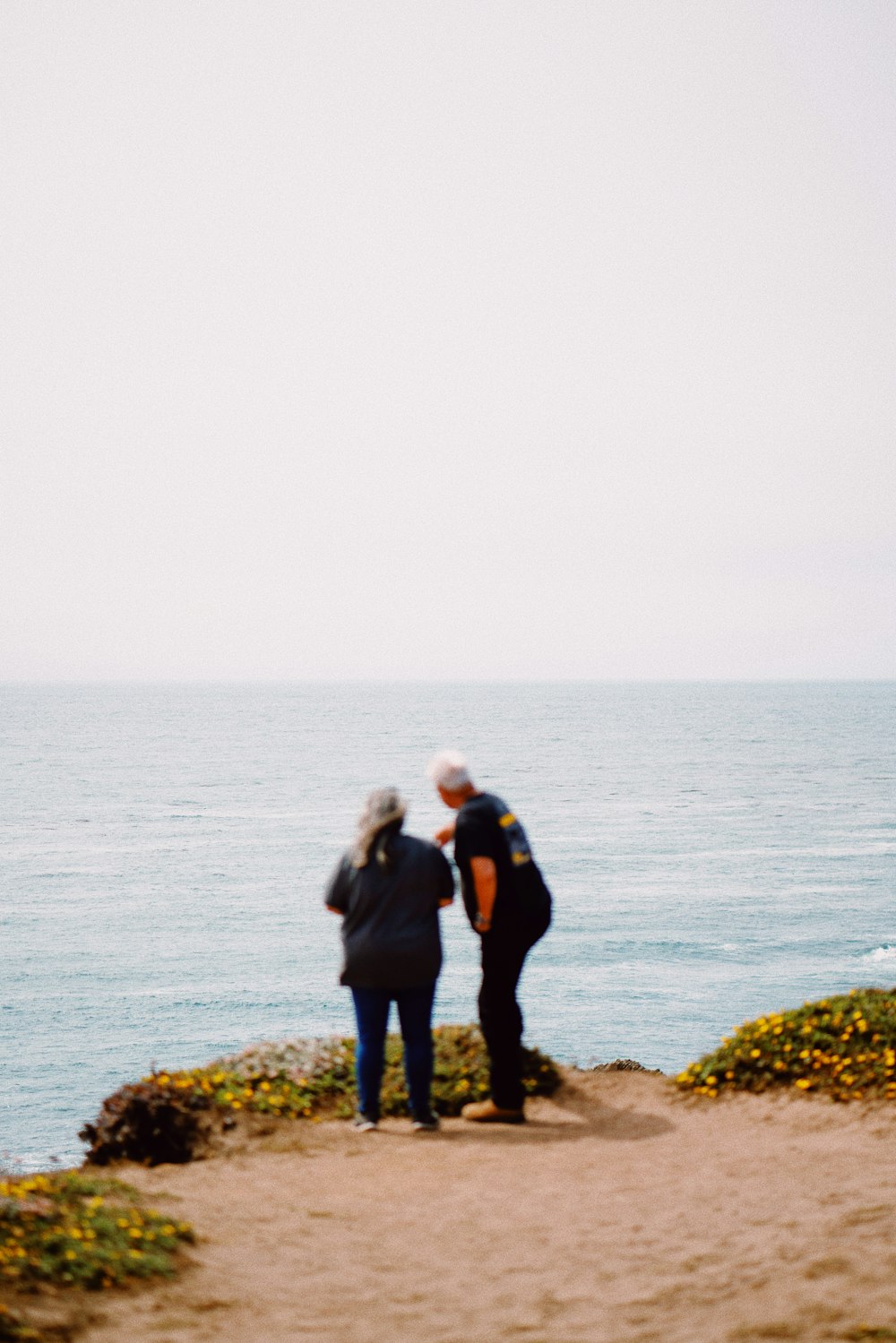 man and woman standing on rock near body of water during daytime