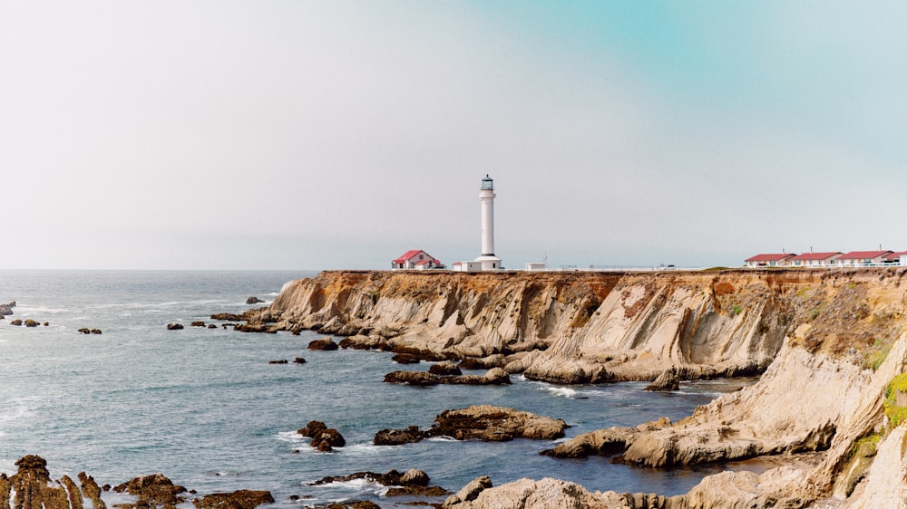 white and red lighthouse on brown rocky mountain beside sea during daytime