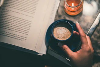 person holding black ceramic mug on white book page