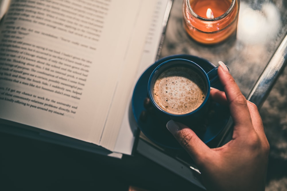 person holding black ceramic mug on white book page