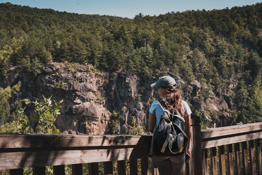 woman in black jacket and blue denim jeans standing on brown wooden fence during daytime