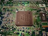 A close-up view of a computer motherboard displaying various electronic components, circuitry, and a central processing unit. The intricately designed circuit patterns are visible, along with soldered connections and small capacitors.