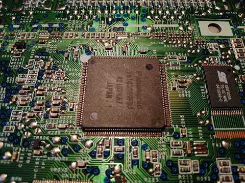 A close-up view of a computer motherboard displaying various electronic components, circuitry, and a central processing unit. The intricately designed circuit patterns are visible, along with soldered connections and small capacitors.