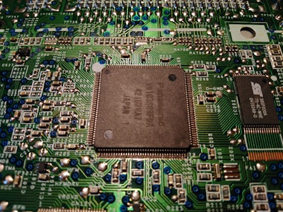 A close-up view of a computer motherboard displaying various electronic components, circuitry, and a central processing unit. The intricately designed circuit patterns are visible, along with soldered connections and small capacitors.