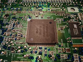 A close-up view of a computer motherboard displaying various electronic components, circuitry, and a central processing unit. The intricately designed circuit patterns are visible, along with soldered connections and small capacitors.