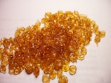 A pile of small, round, translucent amber-colored resin pieces spread across a white surface with text barely visible underneath.