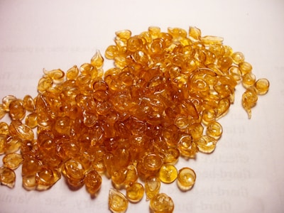 A pile of small, round, translucent amber-colored resin pieces spread across a white surface with text barely visible underneath.