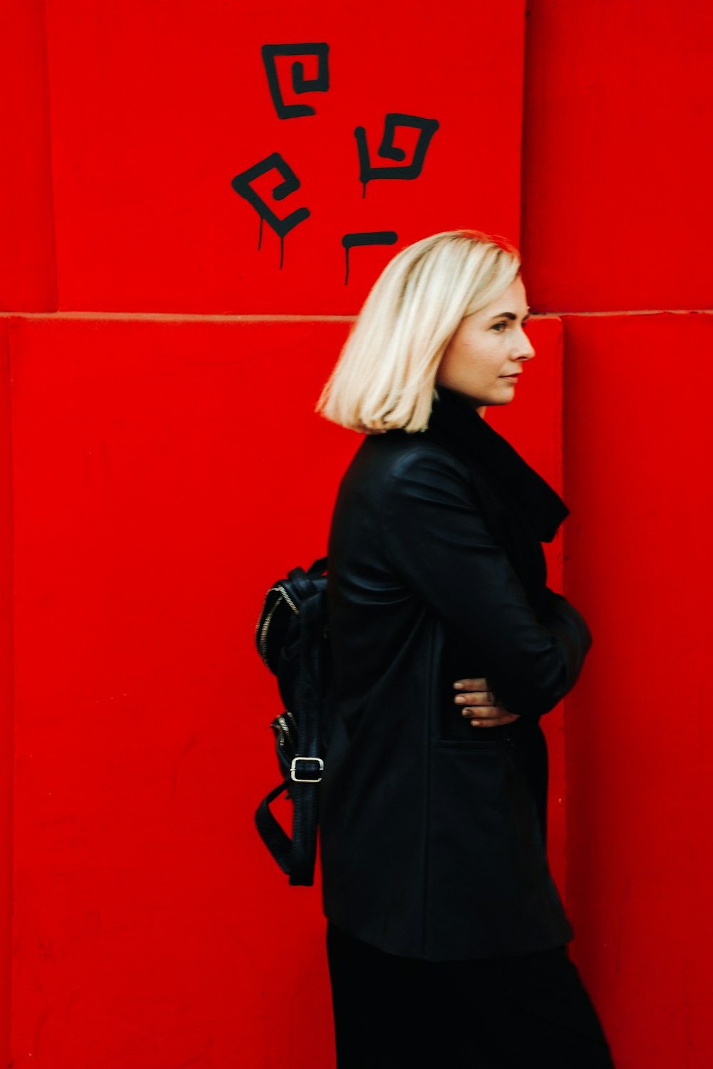 woman in black coat standing beside red wall