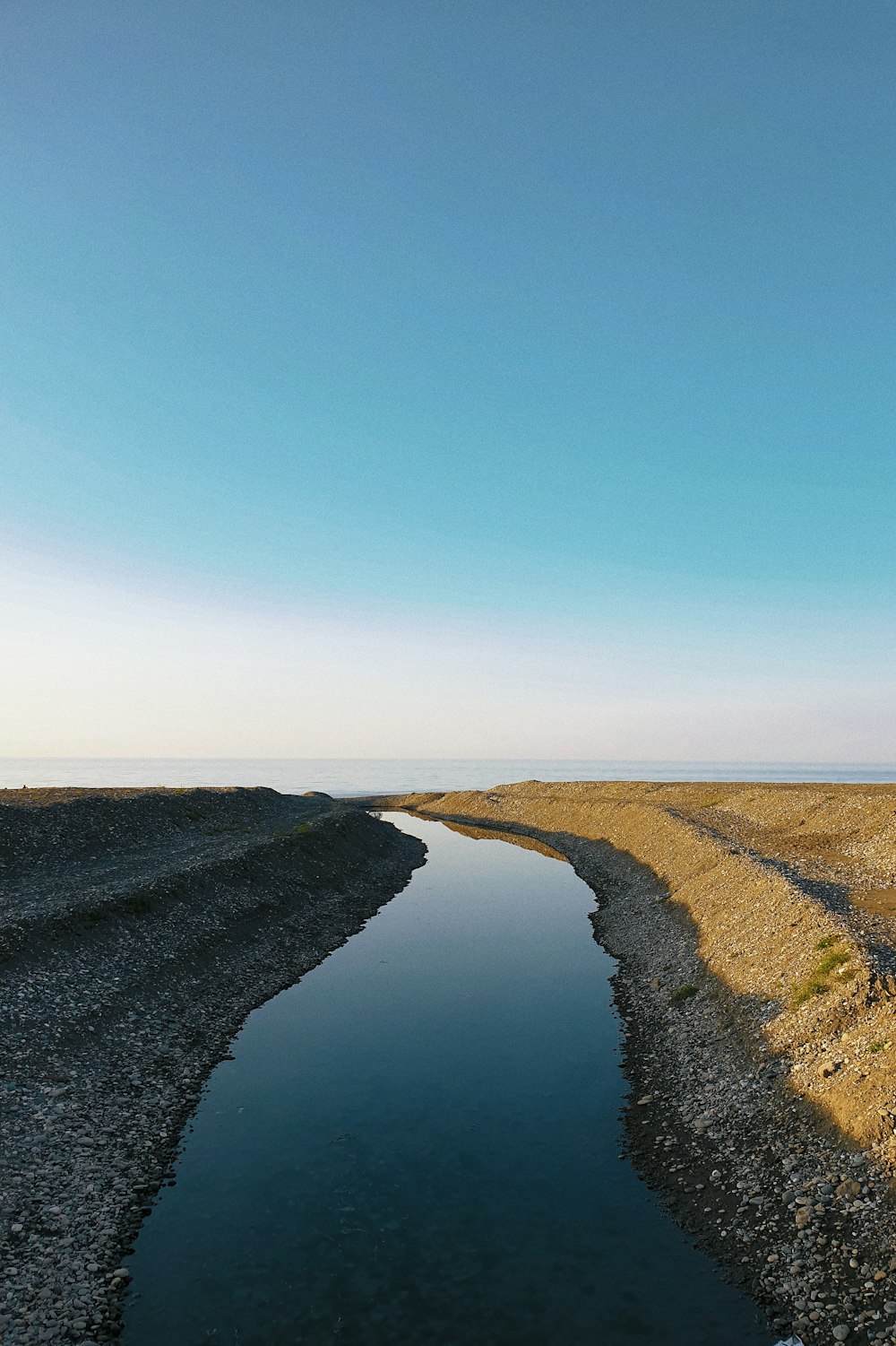 a body of water sitting in the middle of a dry grass field