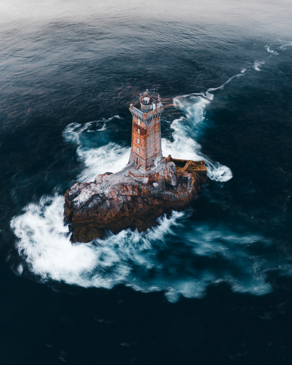 Faro de hormigón marrón y blanco en formación rocosa marrón en medio del mar