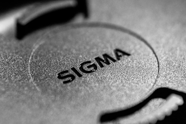 A close-up image of a textured surface featuring the word 'SIGMA' embossed in bold letters. The surface appears to be made of metal with a circular design element in the center.