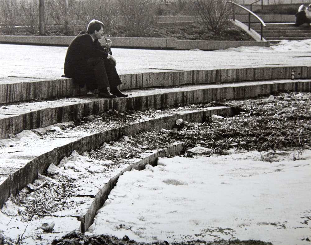 man in black jacket and black pants sitting on concrete stair during daytime