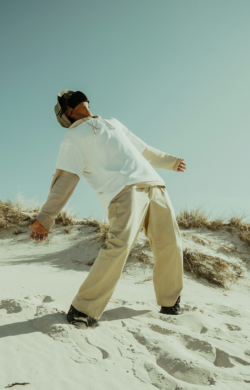 man in white long sleeve shirt and pants standing on white sand during daytime