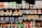 A grocery store shelf filled with a wide variety of colorful beverages in cans and bottles. The products include coconut water, carbonated soft drinks, teas, and fruit-flavored drinks. The packaging features vibrant colors and different languages.