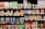 A grocery store shelf filled with a wide variety of colorful beverages in cans and bottles. The products include coconut water, carbonated soft drinks, teas, and fruit-flavored drinks. The packaging features vibrant colors and different languages.